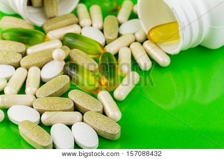 Mixed natural food supplement pills omega 3 calcium multivitamin and glucosamine capsules on green background