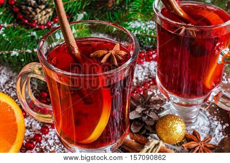 two glasses of hot mulled wine with spices and sliced orange on wooden background with christmas decorations. close up