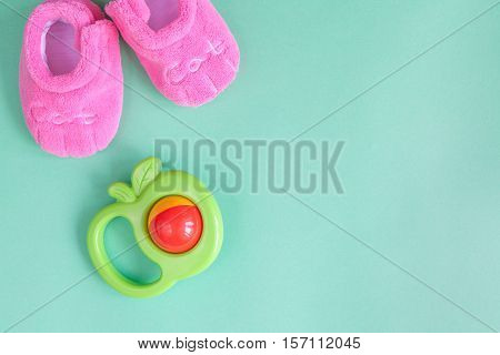 baby rattle and booties on green background top view