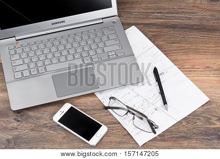 Minsk, Belarus - April 16, 2016: Business concept. Laptop Samsung Series 7 Ultra OS Windows 8.1, 10 and Apple iPhone 5S on table with documents, Sunglasses. Apple Inc. and Samsung Group.