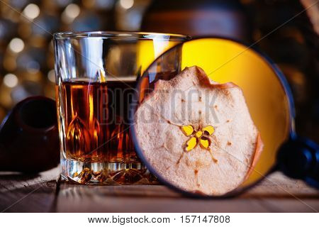 Glass of whiskey, magnifying glass, dried apple and smooking pipe