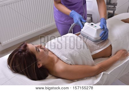 Pretty young woman getting cryolipolyse treatment in cosmetic cabinet