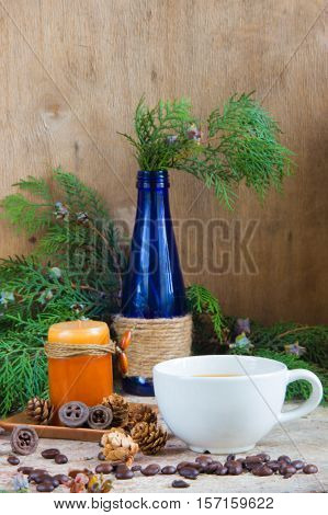 White cup of coffee roasted coffee beans candle blue glass bottle and Christmas tree branch decor on the wooden background