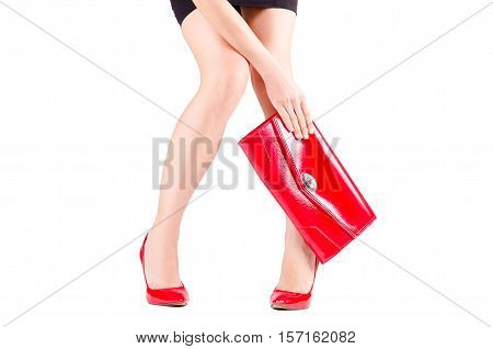 Slender beautiful female legs in red shoes and mini bag in hand isolated on white background