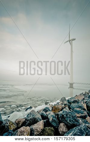modern white wind turbine for generation of renewable electricity in Dutch winter landscape along the IJsselmeer