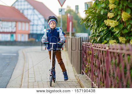 Active school kid boy in safety helmet riding with his scooter in the city. Happy child in colorful clothes biking on way to school. Safe way for kids outdoors to school.