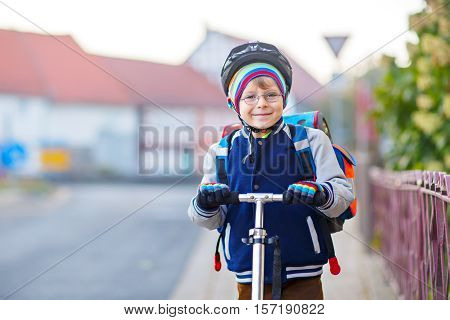 Active school kid boy in safety helmet riding with his scooter in the city. Happy child in colorful clothes biking on way to school. Safe way for kids outdoors to school.
