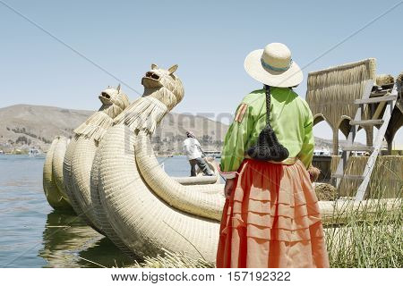 Traditionally dressed Aymara woman looking at the boatman reaching toward her. October 16, 2012 - Uros Floating Islands, Lake Titicaca, Peru