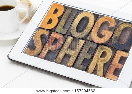 blogosphere (global blog community) word abstract in vintage letterpress wood type on a digital tablet with a cup of coffee