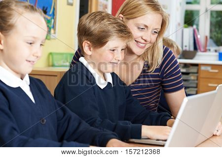 Teacher Helping Elementary School Pupils In Computer Class