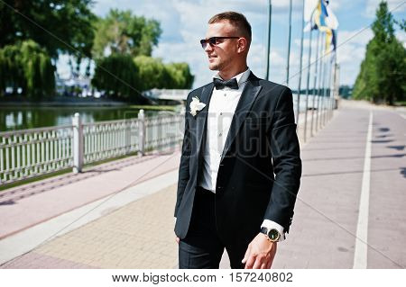 Elegant Groom On Sunglasses Walking Waterfront Of Lake With Flag Mock Up At Sunny Wedding Day.