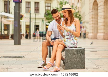 A beautiful young couple are sitting and using a smartphone at the Egyetem Square in Budapest, Hungary.