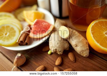 traditional medicine, healthcare and ethnoscience concept - ginger, citrus fruits, tea or honey on wooden table