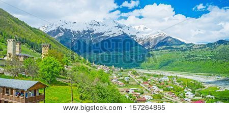 The valley of Mestiachala river with the houses and towers of Mestia surrounded by farm lands and snowy Banguriani Mountain range Upper Svaneti Georgia.