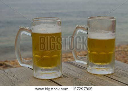 Thw glasses of beer on the wooden table near sea