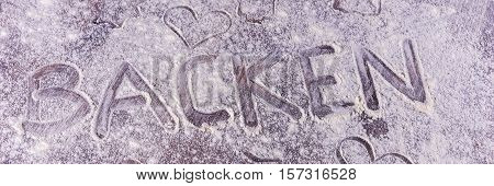 Baking (Backen) in German letters written in flour on the table