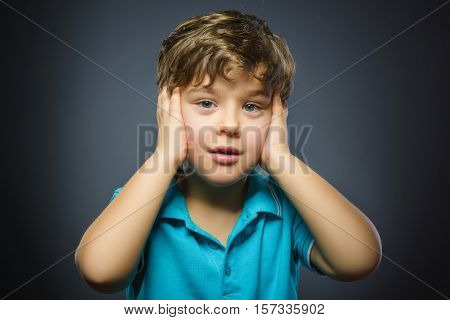 Closeup Portrait of handsome boy with astonished expression while standing against grey background.