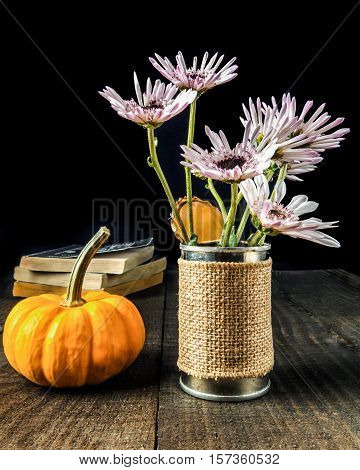 Flowers in krafted vase with pumpkin and old books on a wooden background.
