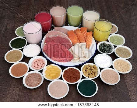 Super food and drinks for body builders with lean meat of steak, chicken and pork with salmon,  dietary supplement powders and vitamin pills on oak background.