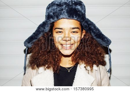 young pretty african american girl teenage outside on street, looking like real junky, social issues concept, red eyes, bum stupid hat, fashion hipster lifestyle people close up mudy