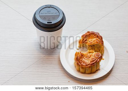 A Chiness moon cake with a hot disposable coffee cup on the wooden table / 2 Chiness capital letters are wish and not trade mark.