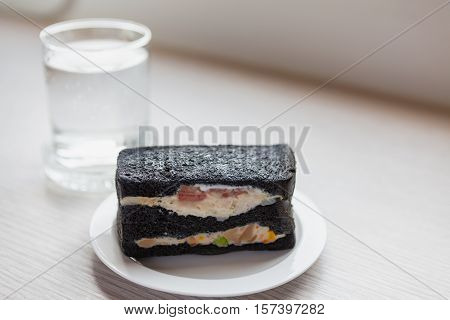 Charcoal sandwiches with Oclock and a glass of dringking water in morning time on wooden table in working room