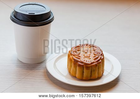A Chiness moon cake with a hot disposable coffee cup on the wooden table / 2 Chiness capital letters are wish and not trade mark.