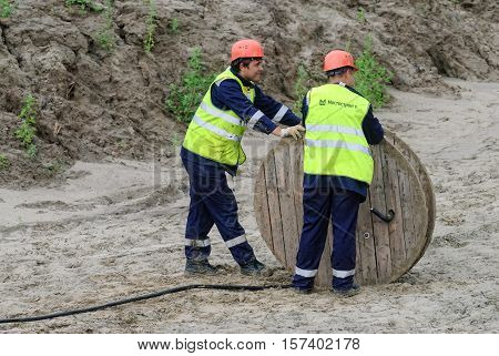 Tobolsk, Russia - July 15. 2016: Sibur company. Construction of plant on processing of hydrocarbons. Two workers pulling roll high voltage cable line