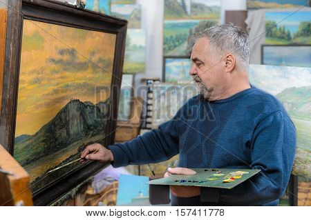 Elderly artist paints a picture oil paints