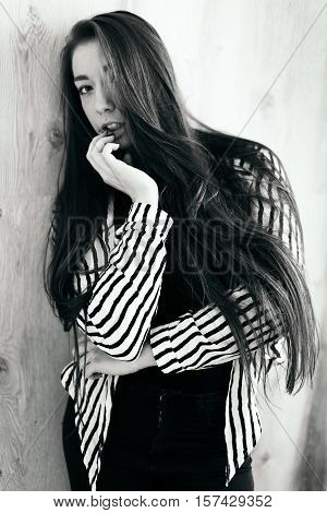 High fashion. Emotional portrait of a beautiful sexy brunette with long hair and bright make-up. Hair is covering half of her face. Portrait in black and white. Wood background.