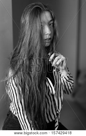 Portrait of a seated girl. Hair is covering half of her face. Portrait in black and white.