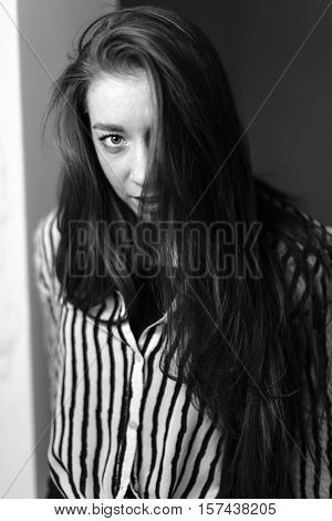 Portrait of a seated girl. Hair is covering half of her face. Portrait in black and white.