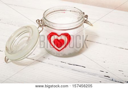 Jar with snow and a heart in him. The white wood background a glass jar a heart from fabric lies in snow