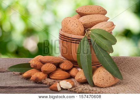 almonds with leaves in a bowl on the old wooden board with blurred garden background.