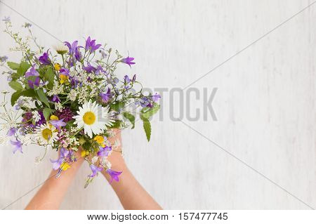 Beautiful bunch of wild flowers in woman's hands on the white wooden background. Flowers from the park. Summer. Gift bouquet.