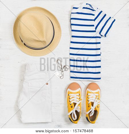 Child's striped t-shirt demin shorts accessories yellow shoes and straw hat isolated on white background. Top view. Flat lay. Kid's summer clothes collage