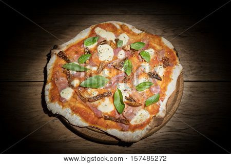 Homemade pizza with figs prosciutto ham and mozzarella cheese on wooden table top view in the dark