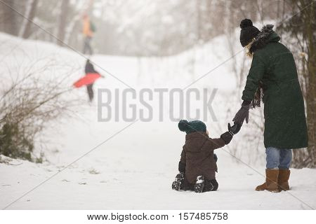 Mother and little toddler boy walking in the winter forest and having fun with snow. Family enjoying winter. Child and woman watching falling snow outdoors. Winter Christmas and lifestyle concept.