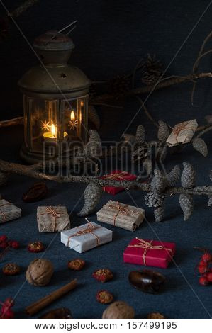 Christmas gifts, rowan, nuts, old lamp and pine branch with cones on dark surface