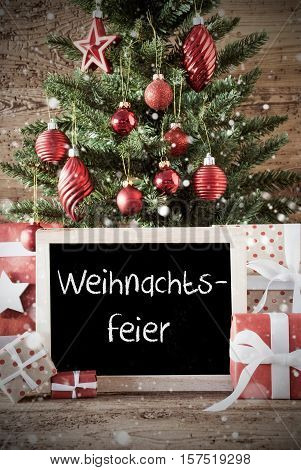 Chalkboard With German Text Weihnachtsfeier Means Christmas Party. Nostalgic Christmas Card For Seasons Greetings. Christmas Tree With Balls. Gifts Or Presents In The Front Of Wooden Background.