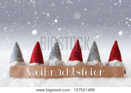 Label With German Text Weihnachtsfeier Means Christmas Party. Christmas Greeting Card With Gnomes. Silver Background With Snow And Snowflakes