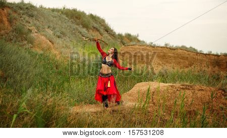 Oriental Beauty dance with a sword. Tribal style. Lovely girl in costume dancing outdoors. Sand dunes. Nomads.