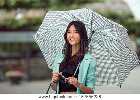 Asian girl city portrait. Woman smiling outside with umbrella in casual business suite looking at camera. Beautiful young mixed race Asian Caucasian woman.
