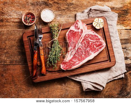 Raw T-bone Steak for grill or BBQ on cutting board over aged wooden background, top view