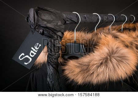 Sale Sign. A Lot Of Black Coats, Jacket With Fur On Hood Hanging  Clothes Rack.  Background.  Friday
