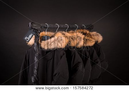 Sale Sign. A Lot Of Black Coats, Jacket With Fur On Hood Hanging  Clothes Rack.  Background.  Friday