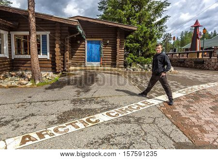 Young man standing on the line of the arctic circle in Rovaniemi Finland.