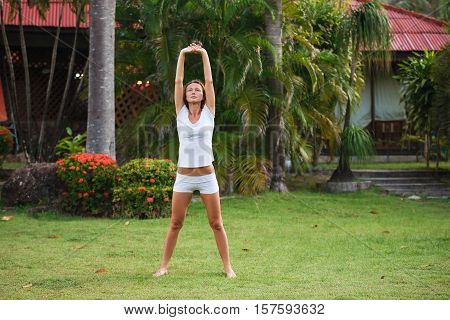 Young beautiful fitness girl with ponytail do exercises on green grass at the park.