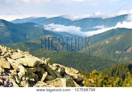 Beautiful landscape of the Carpathian mountains in autumn. Day. Large stones against the hill covered with pine forest creeping pine and fluffy white clouds