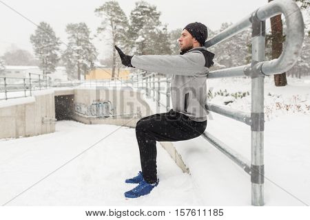 fitness, sport, people, exercising and healthy lifestyle concept - young man doing squats and warmig up at fence in winter